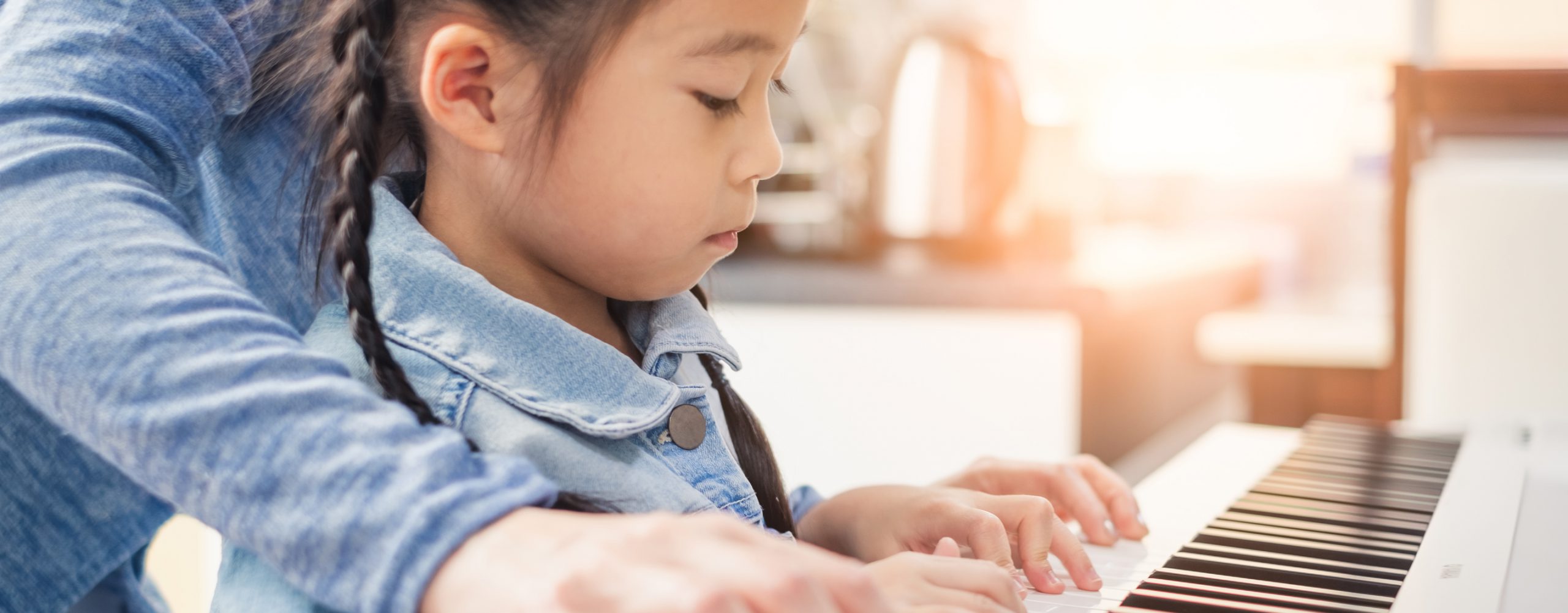 Child learning piano with adult guidance at a keyboard in a bright home setting